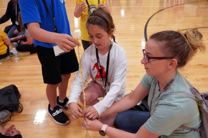 A Purdue College of Education student helping two schoolchildren build a tower out of pasta.