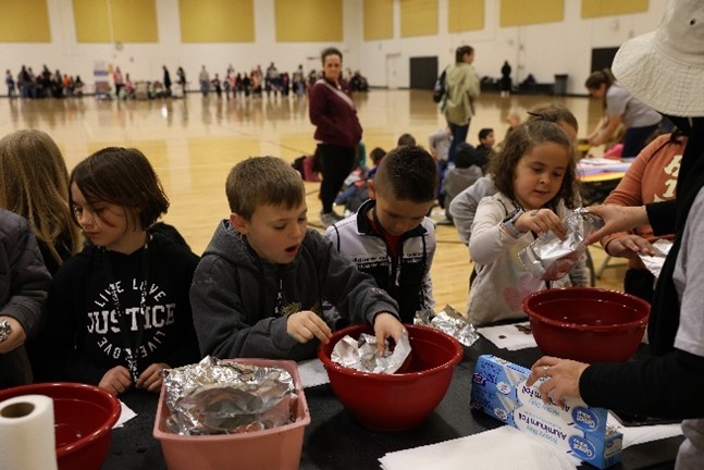 Several schoolchildren creating floating structures out of aluminum foil to hold the most coins before sinking in the water.