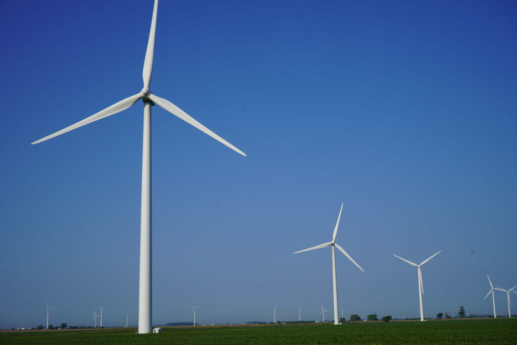 A series of wind turbines in front of a blue sky and green field.