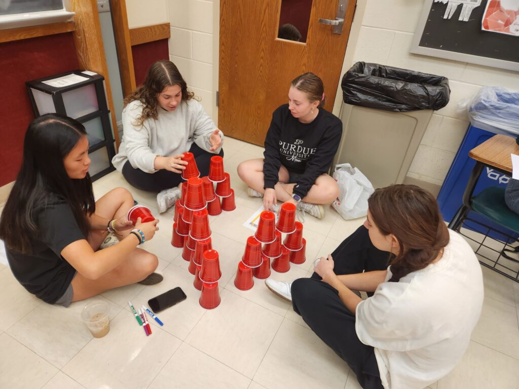 A group of students work together on a cup stacking activity