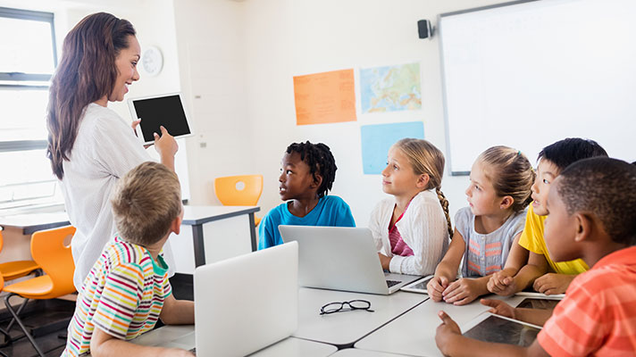 A female teacher points to a tablet in front of a group of students