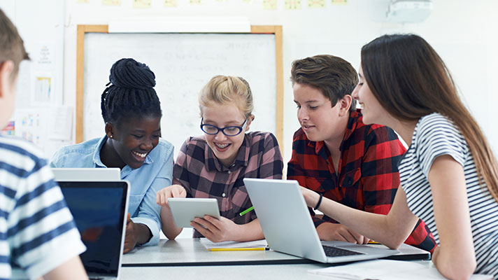 A group of students work on laptops and tablets in a classroom