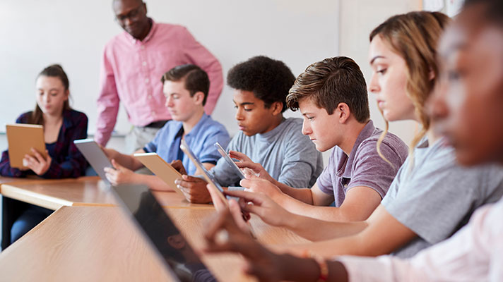 A teacher oversees a group of students working on tablets