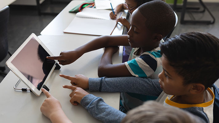 Two elementary students work on a tablet in a classroom.
