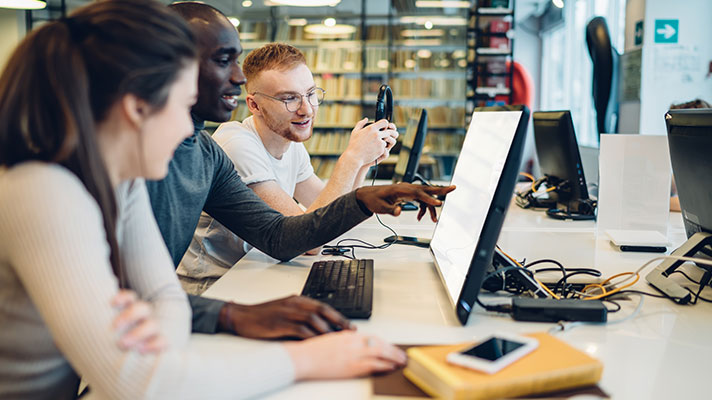 Three students work on a project in a computer lab in the library