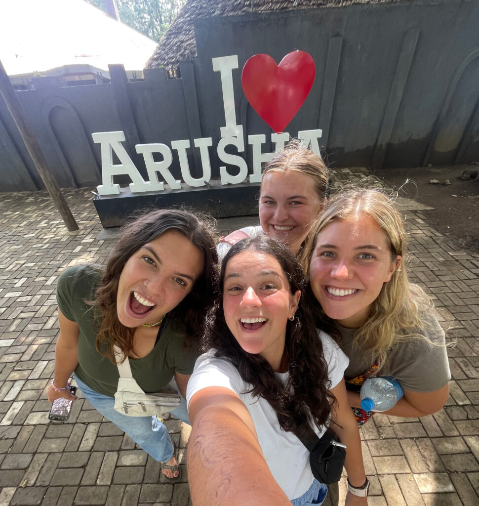 Four college aged students taking a selfie in front of an "I Love Arusha" sign.
