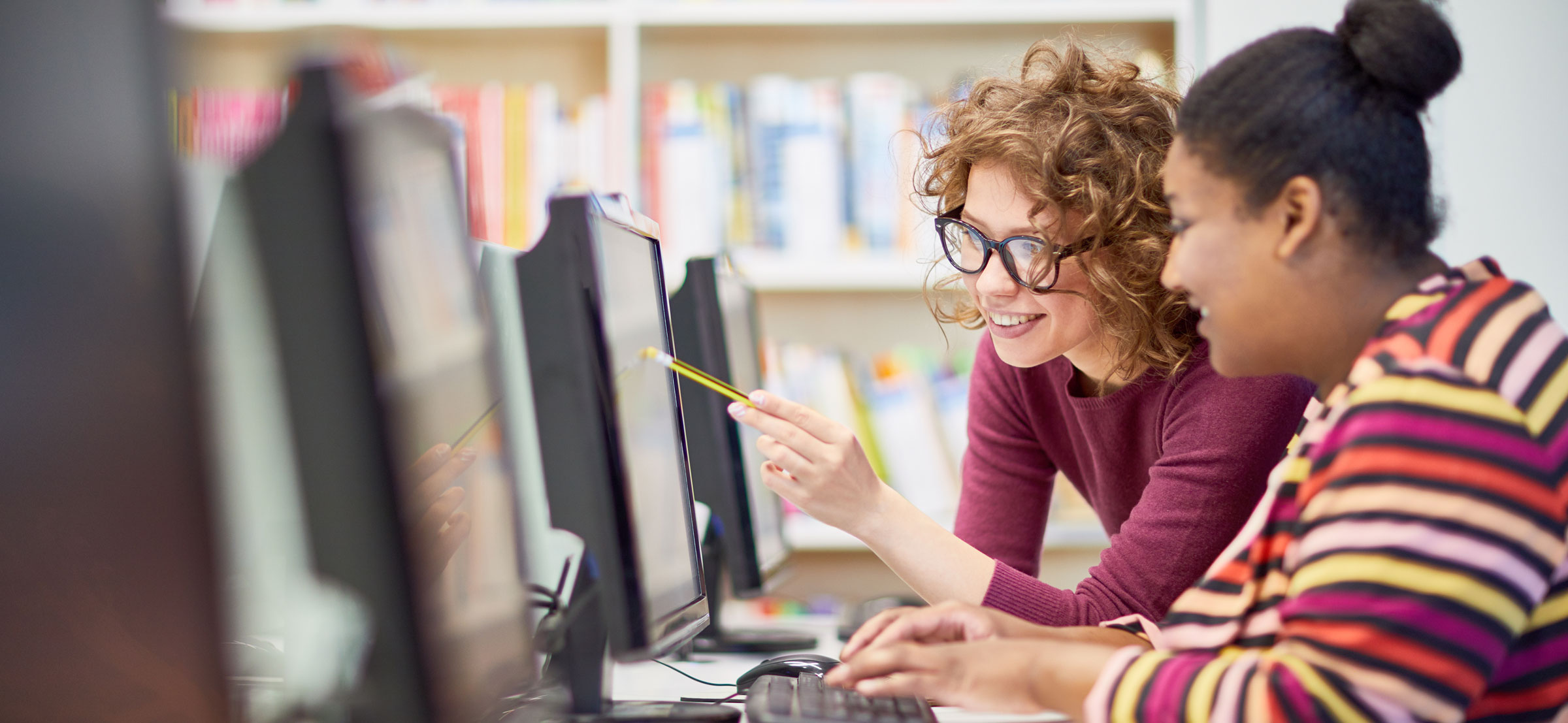 A white female and a black female work together on a computer.