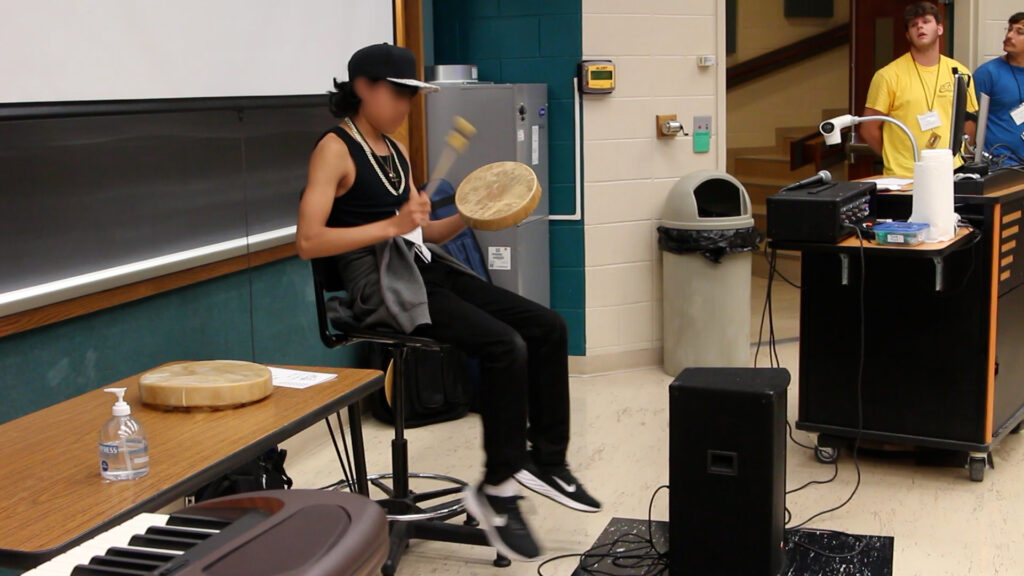 A student drumming in front of a classroom