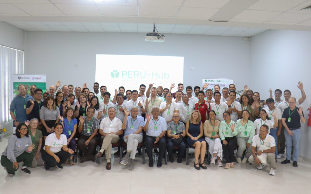 A large group of PERU-Hub staff and international partners smiling and waving.
