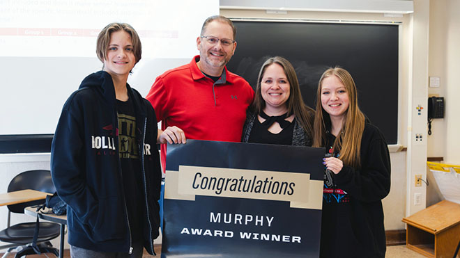Jennifer Smith holding up a sign that says, "Congratulations Murphy Award Winner". She is surrounded by three of her family members.