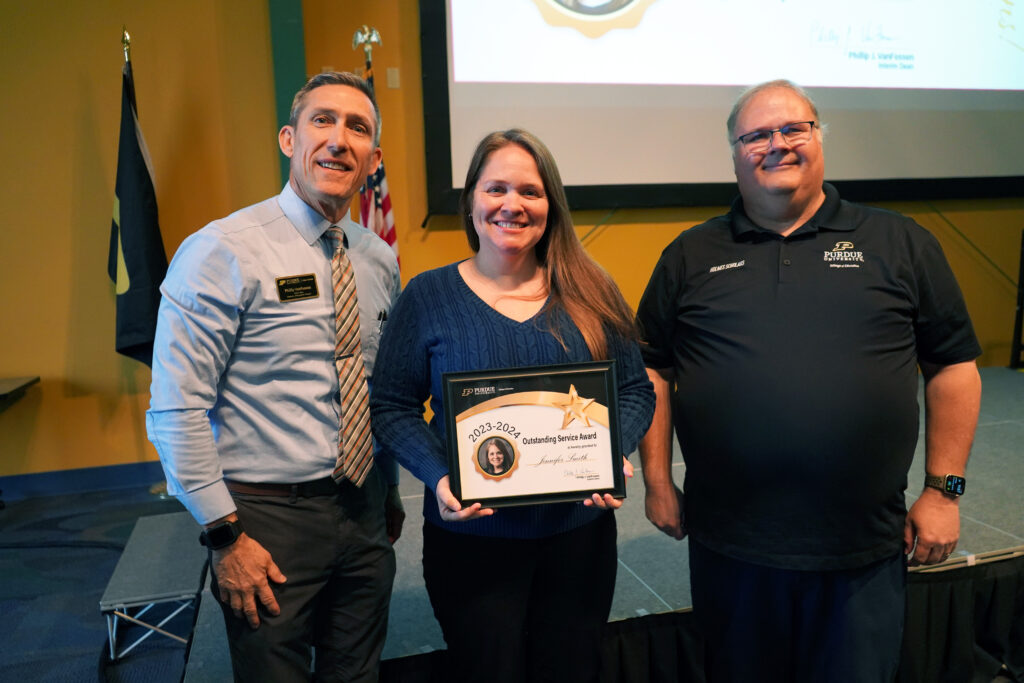Jennifer Smith holding a certificate for the 2023-2024 Outstanding Service Award. Beside her are Interim Dean VanFossen and Wayne Wright