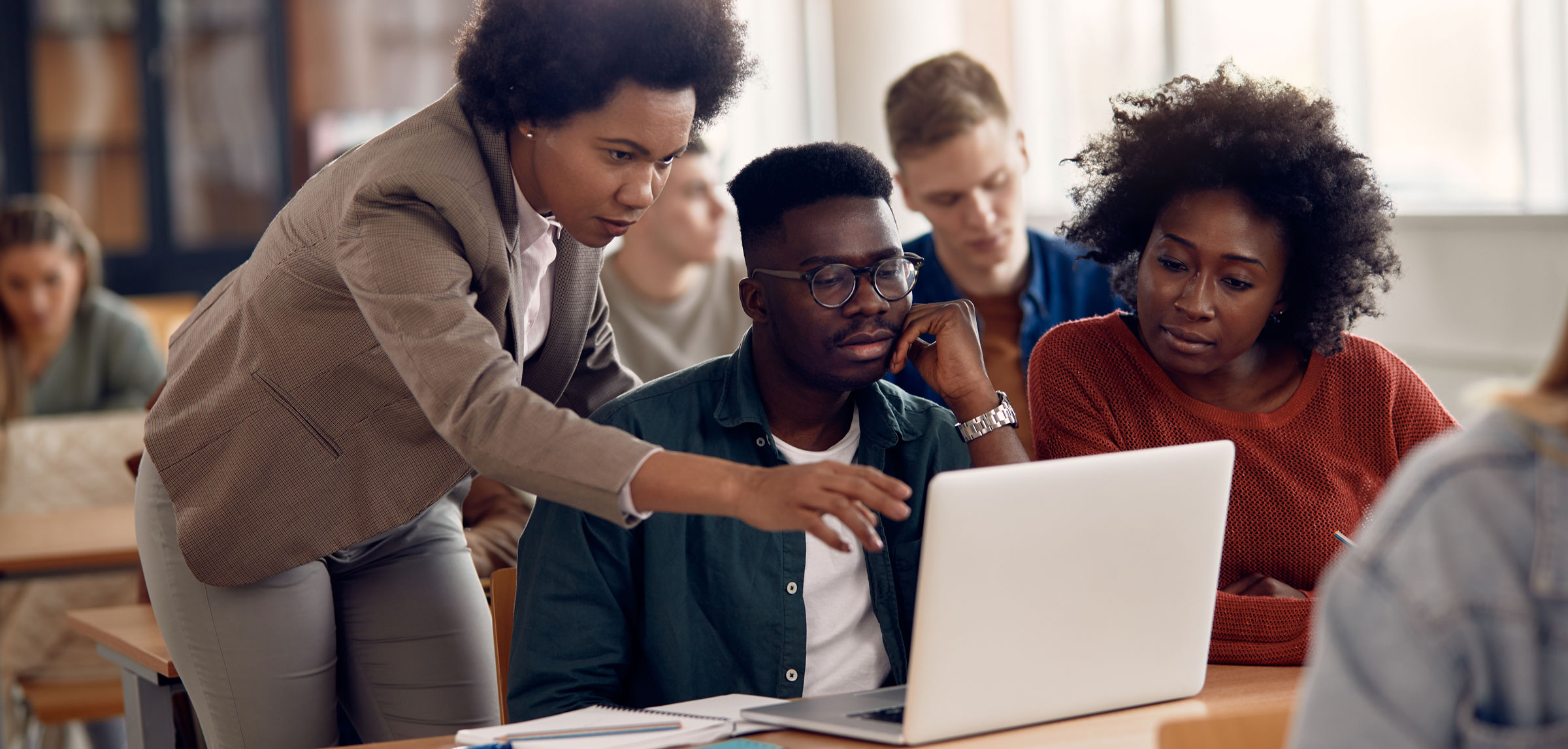 A black female helps a black male and black female with something on their computers