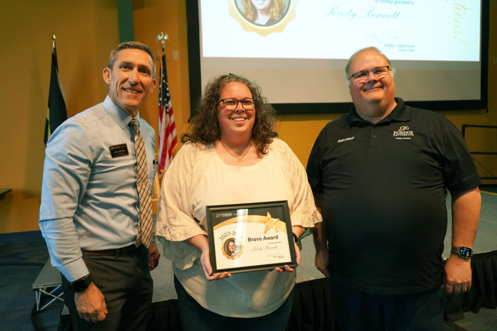 Kristy Bennet holding a certificate for the 2023-2024 Bravo Award. Beside her are Interim Dean VanFossen and Wayne Wright