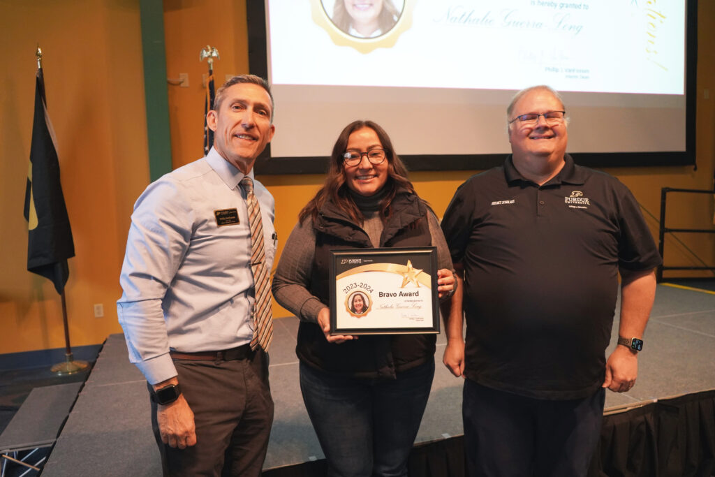 Nathalie Guerra Long holding a certificate for the 2023-2024 Bravo Award. Beside her are Interim Dean VanFossen and Wayne Wright
