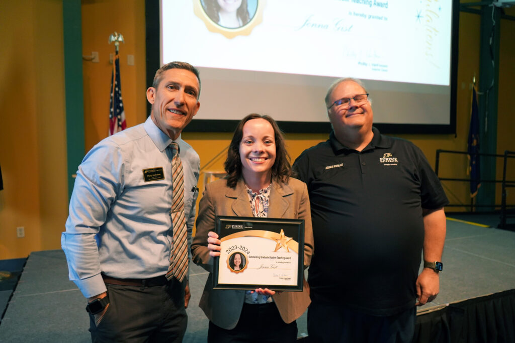 Jenna Gist holding a certificate for the Outstanding Graduate Student Teaching Award. Beside her are Interim Dean VanFossen and Wayne Wright