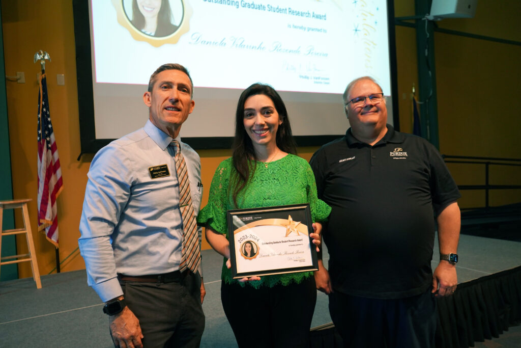 Daniela V Resende Pereira holding a certificate for the Outstanding Graduate Student Research Award. Beside her are Interim Dean VanFossen and Wayne Wright