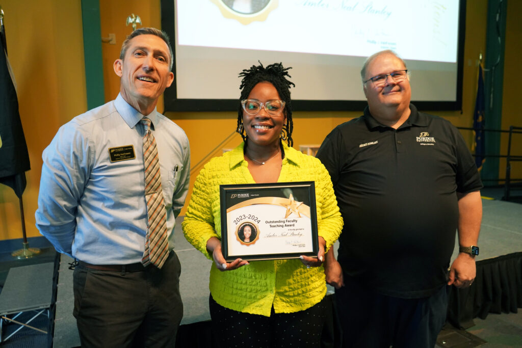 Amber Neal-Stanley holding a certificate for the Outstanding Faculty Teaching Award. Beside her are Interim Dean VanFossen and Wayne Wright