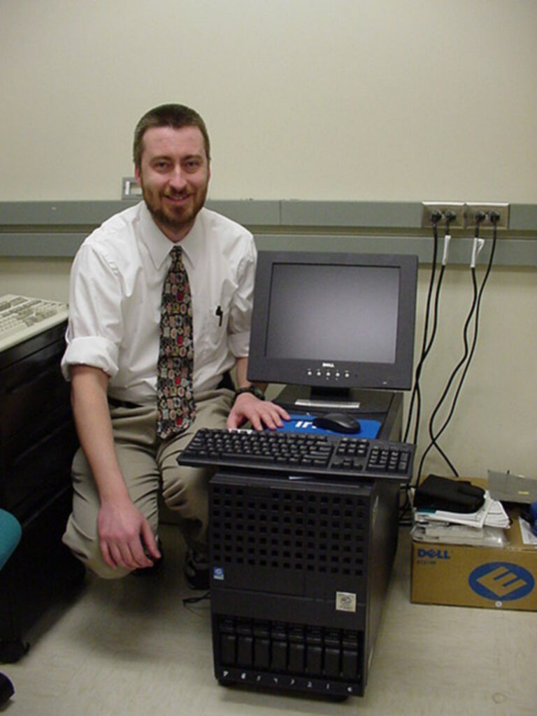 Bob Evans sitting next to a computer server, monitor, and keyboard.