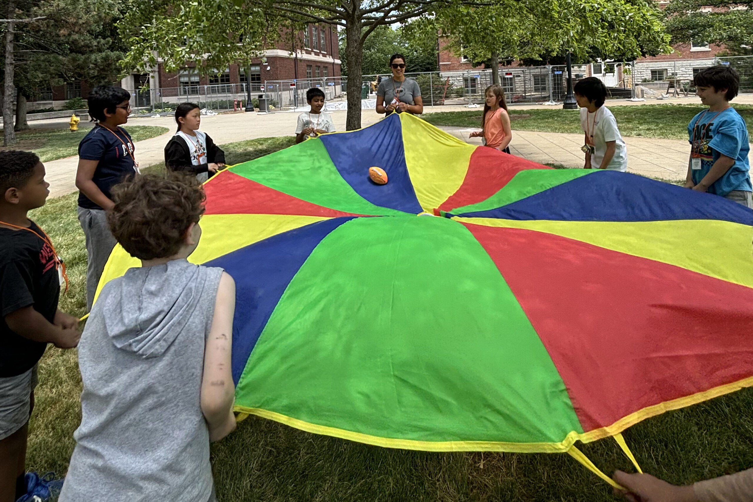 A group of GER2I students playing a teambuilding activity outside. Each student is holding a handle of a large circular colorful sheet.