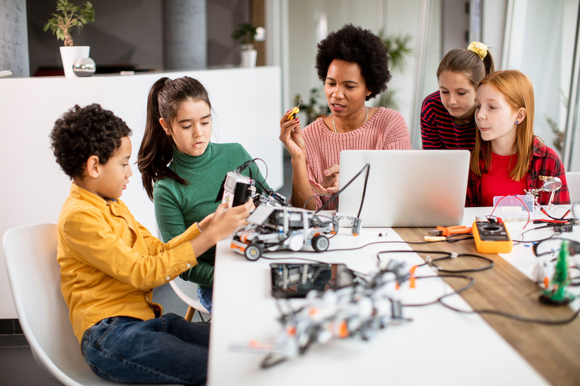 A black female teacher works with a group of students using computers and robotics