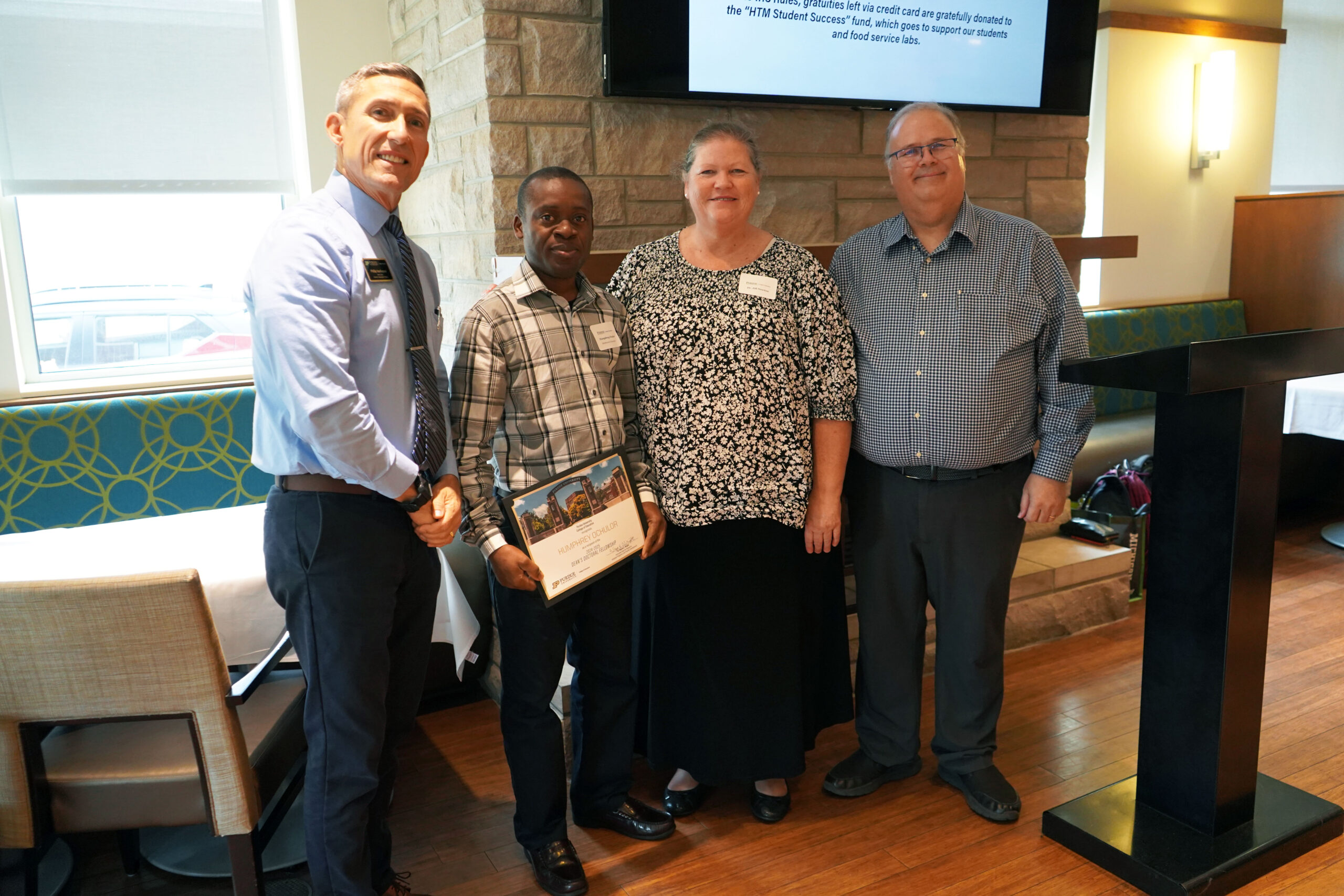 Humphrey Ochulor holding a certificate. Surrounding him are interim dean Phillip J. VanFossen, Dr. Jill Newton, and Dr. Wayne Wright.