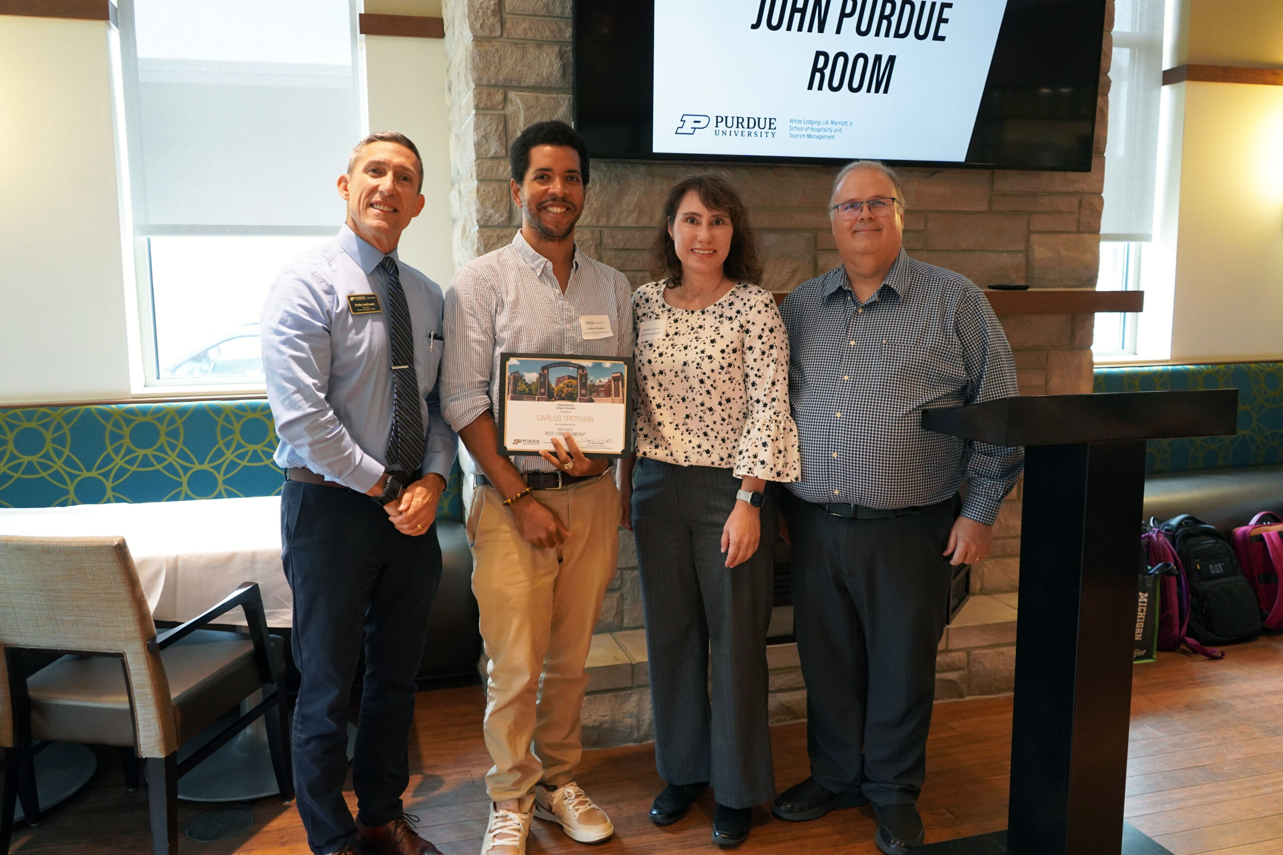 Carlos Trotman holding a certificate. Surrounding him are interim dean Phillip J. VanFossen, Dr. Victoria Lowell, and Dr. Wayne Wright.