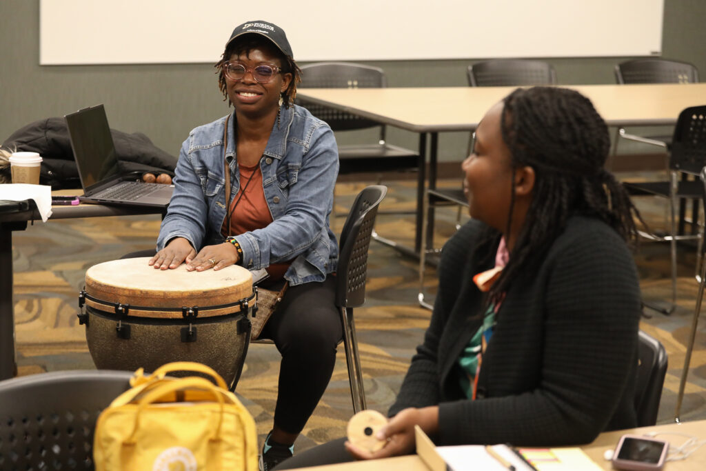 Two ICLCLE attendees playing a drum-like instrument.