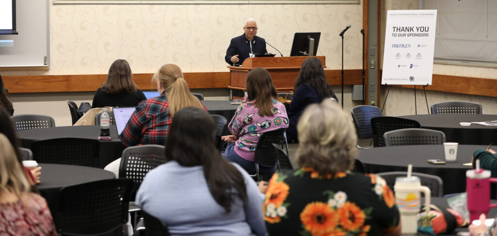 Dr. Serafín M. Coronel-Molina standing at a podium, speaking to a group of seated ICLCLE attendees.