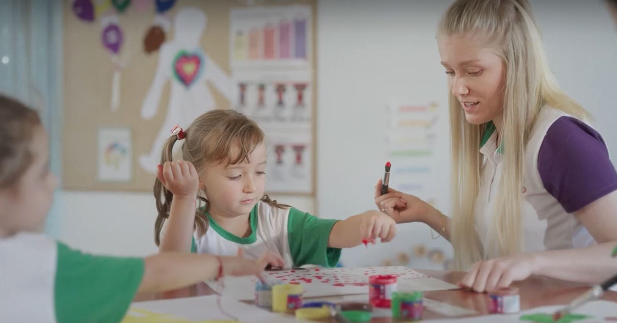 A young female teacher painting with two young children in a classroom.