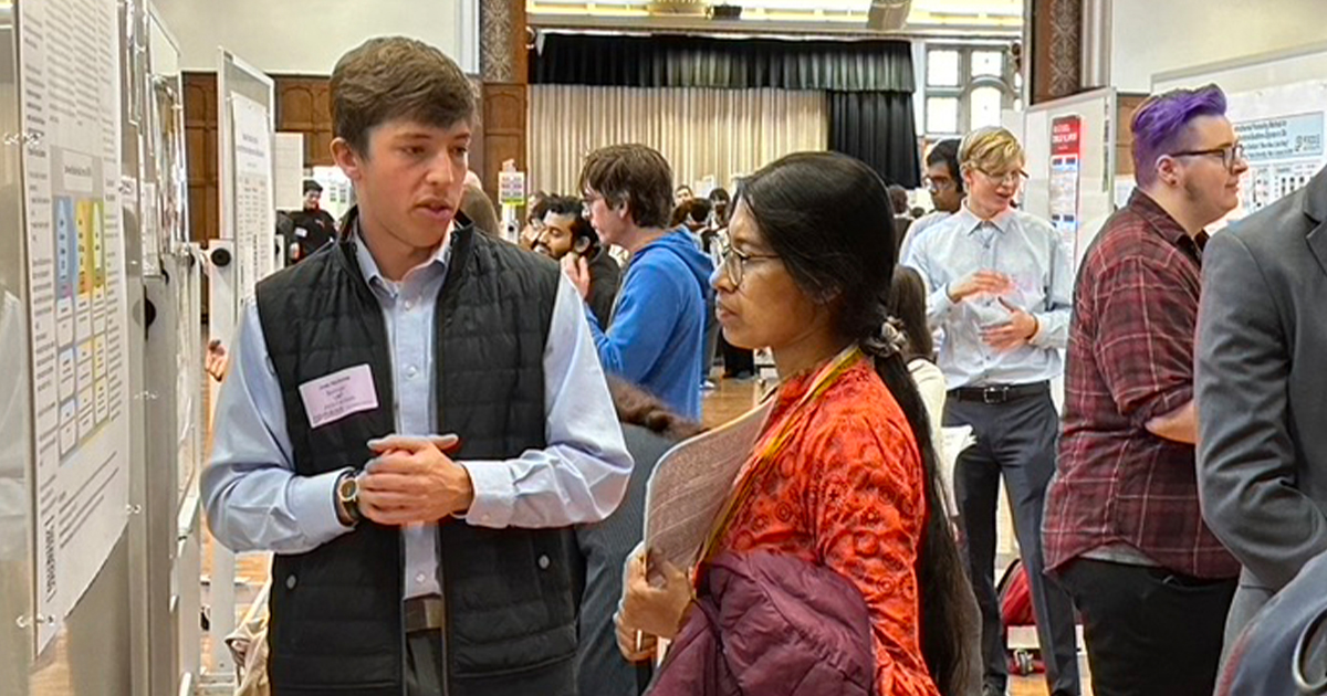 A male student presenting his poster to a viewer.