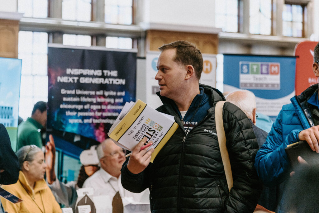 A conference attendee holding a brochure and looking to his side.