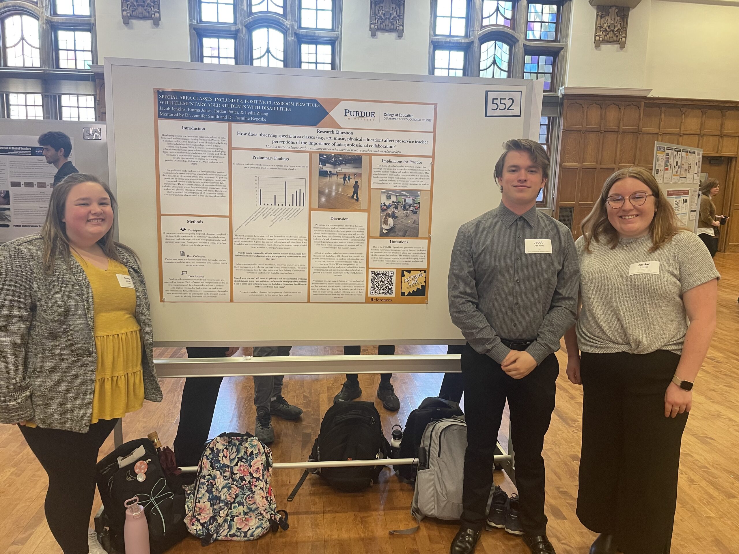 Three students stand with a research poster in a large hall