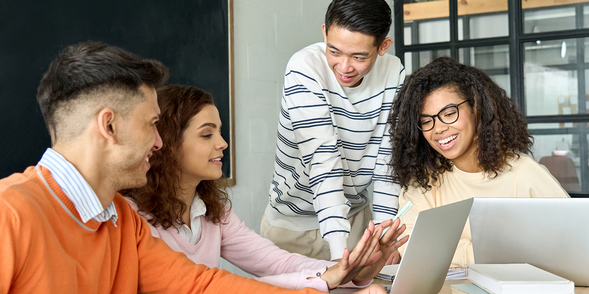 A group of four college age students in a classroom working on project using laptops.