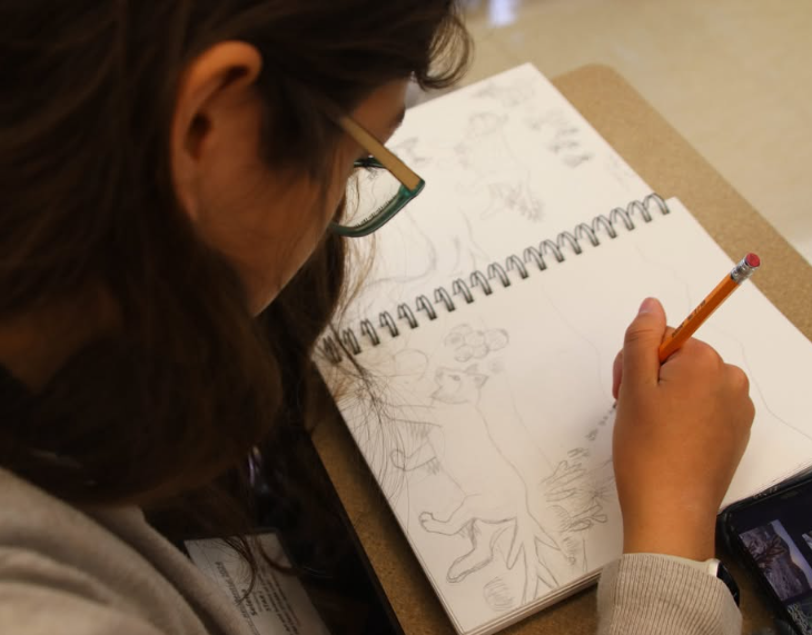 A sketchbook is shown over a student's shoulder
