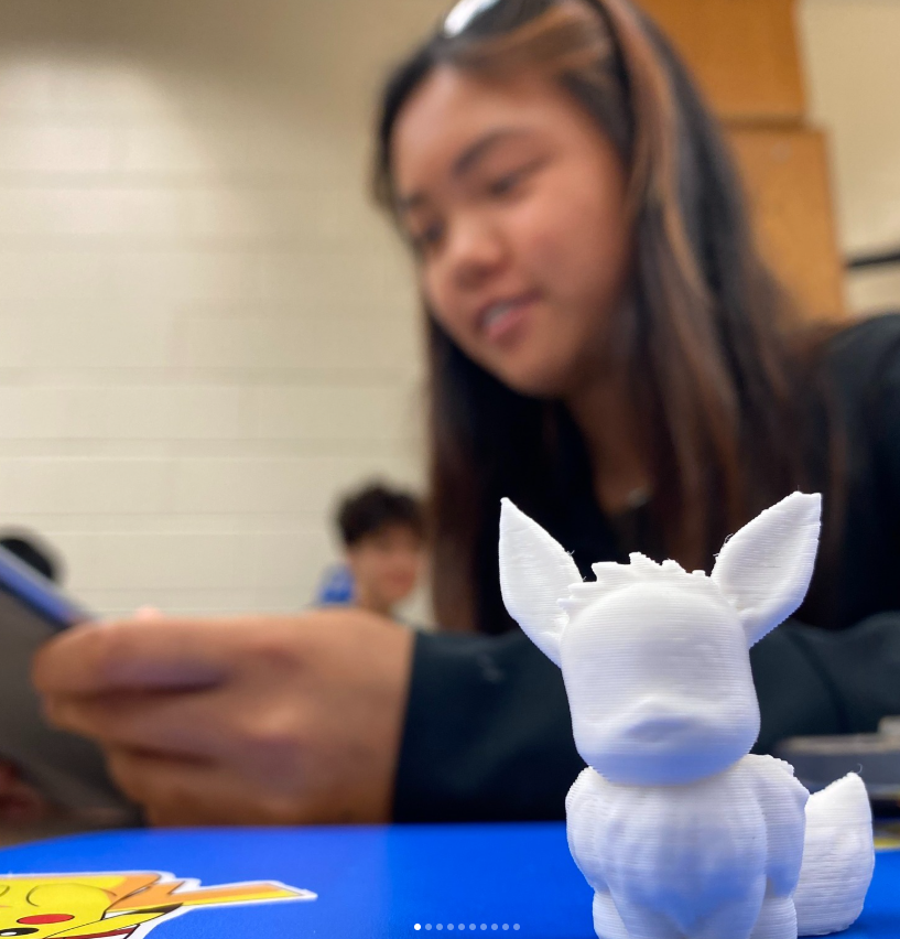 A 3D printed character sits on a table with a student blurred behind it