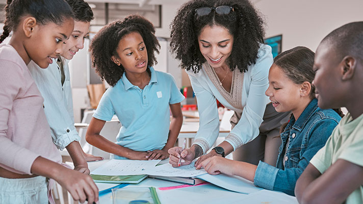 A teacher points out something in a book to a group of students