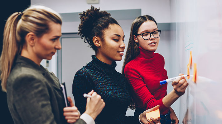 Three students collaborate on a project on a whiteboard