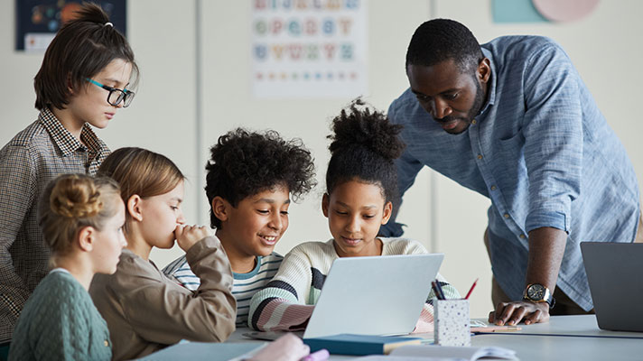 A teacher looks over a student's shoulder while they work on a project