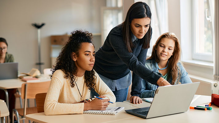 An instructor points out something on a laptop to two students