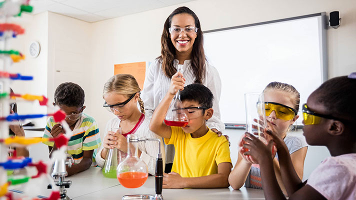 A teacher works with students using science beakers