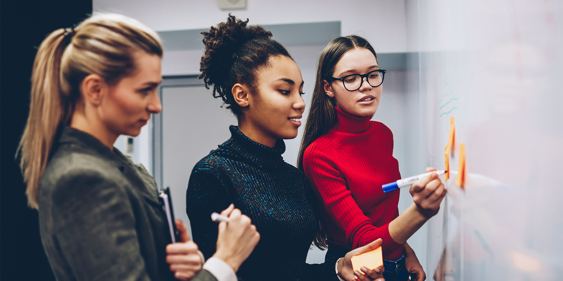 Three students collaborate on a project on a whiteboard