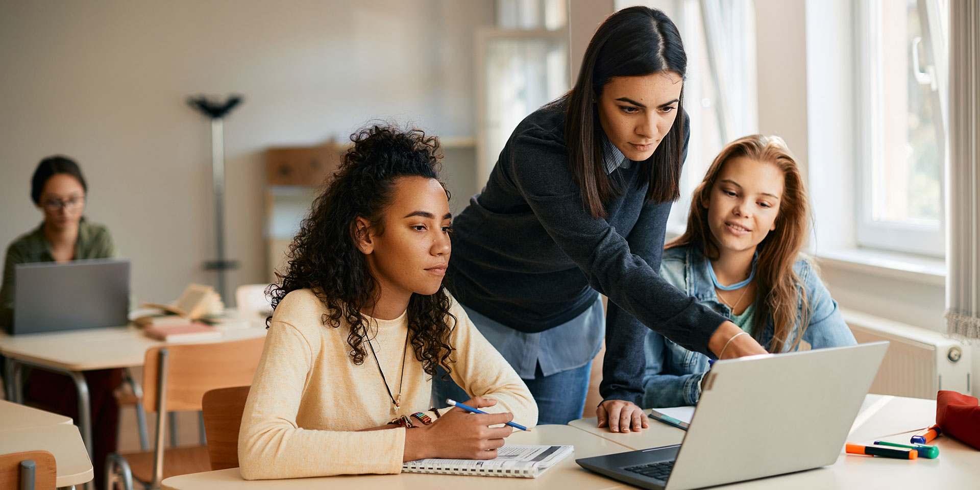An instructor points out something on a laptop to two students