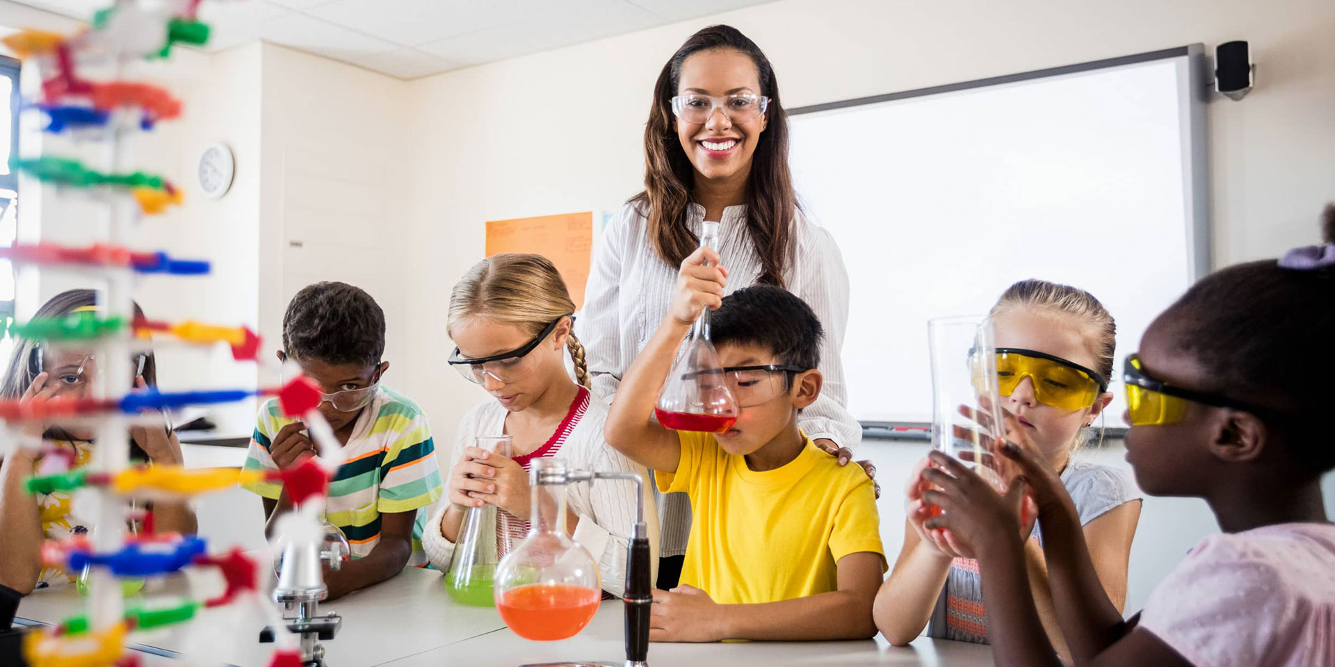 A teacher works with students using science beakers