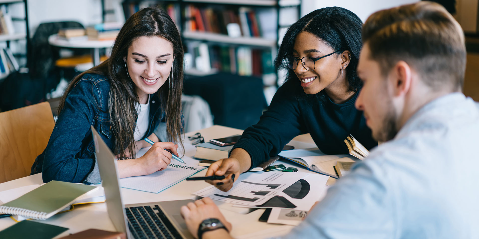 Students work on a project on a laptop in a library.