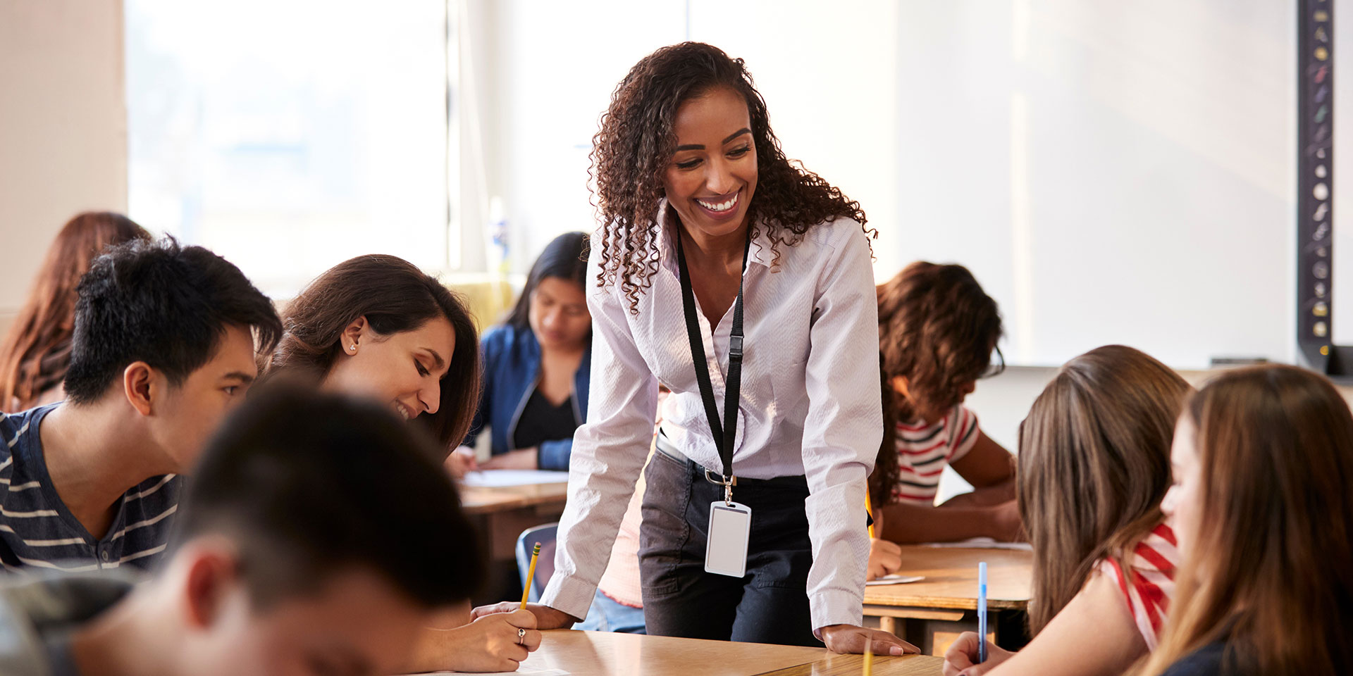 A teacher leans over a desk talking with students