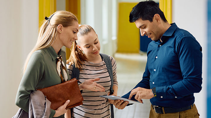 A male school administrator talks with a parent and student in a school hallway