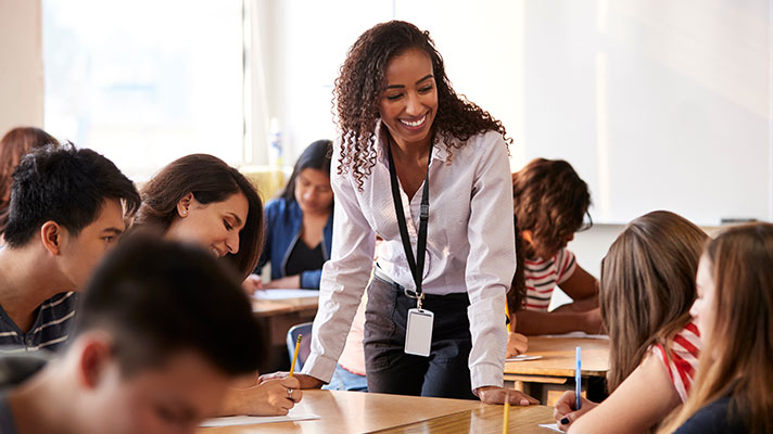 A teacher leans over a desk talking with students