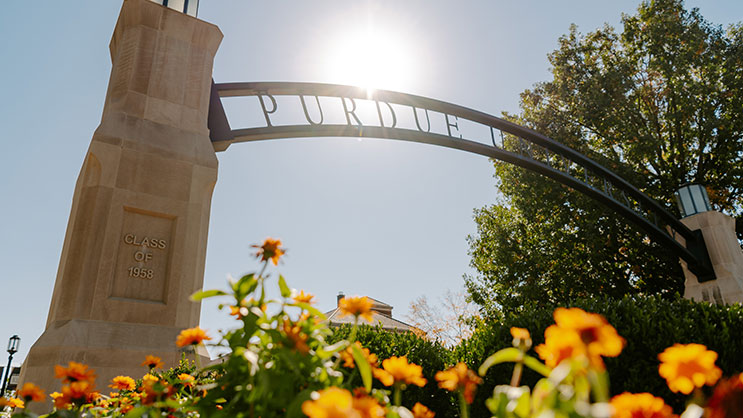 A ground level view of the Purdue University arch. In the foreground is a bush of orange flowers.