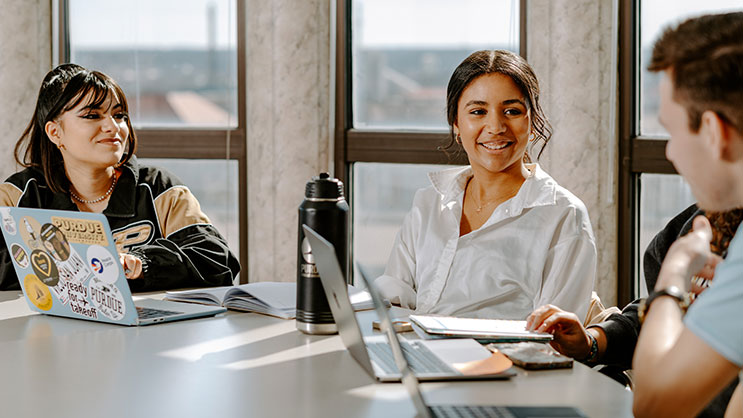A group of college students seated at a table. In front of them are laptops, water bottles, and notebooks.