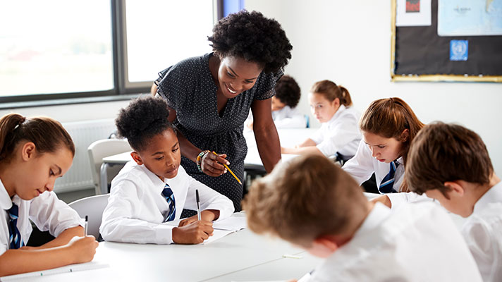 A female teacher points out something to a student over their shoulder